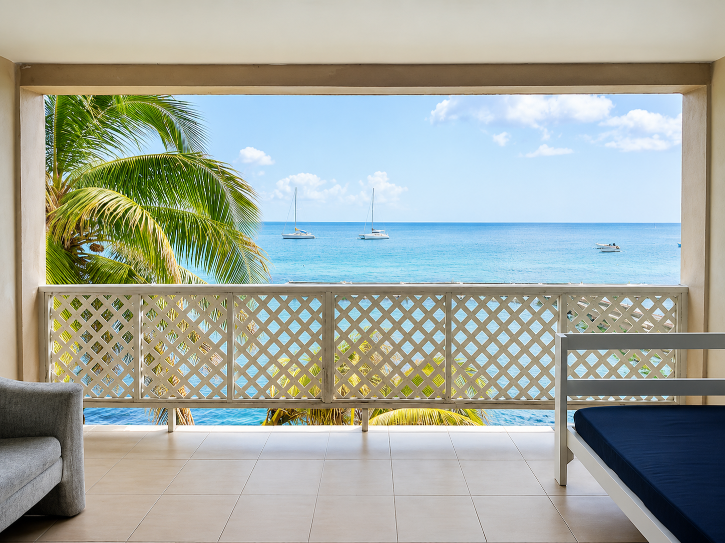 Private balcony with a daybed and palm tree overlooking the Caribbean Sea, sailboats on the water at Point Bay Resort