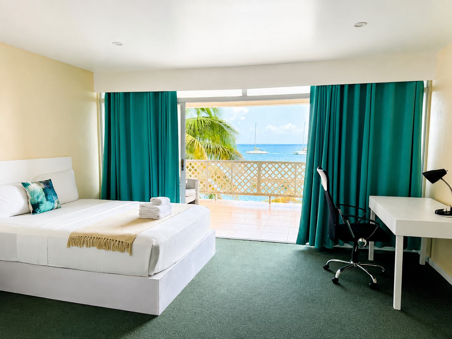 Ocean View room with a queen bed, white linens, a turquoise throw cushion, teal curtains and a private balcony overlooking the Caribbean Sea